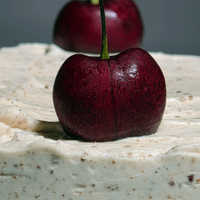 Close-up of a fresh cherry on chocolate-flecked cream frosting on a white forest cake